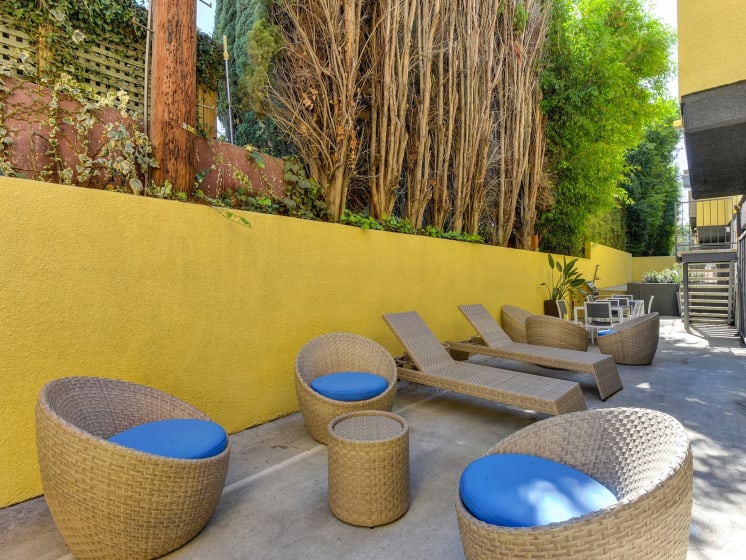 Community Lounge Area with Wicker Seats with Blue Cushions, Wicker Lounge Chairs, Trees, and Yellow Wall